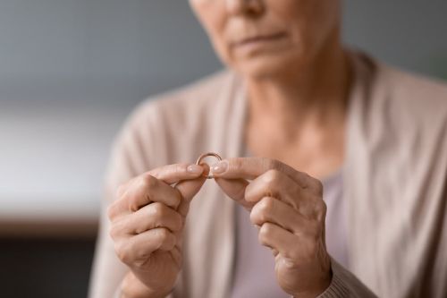 Unhappy unrecognizable senior widow woman holding wedding ring indoors, cropped