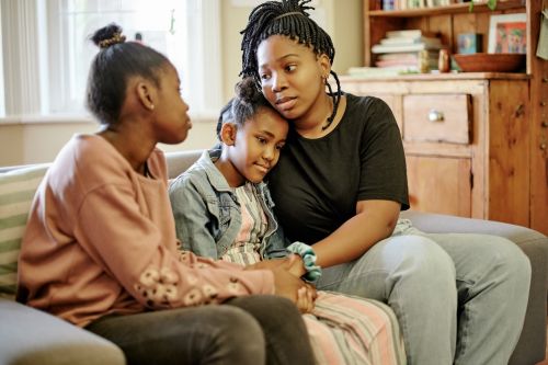 Love, comfort and children with mother on a sofa holding hands, hug and sharing compassion in their home. Family, support and mom with unhappy kids in living room for help, understanding and empathy